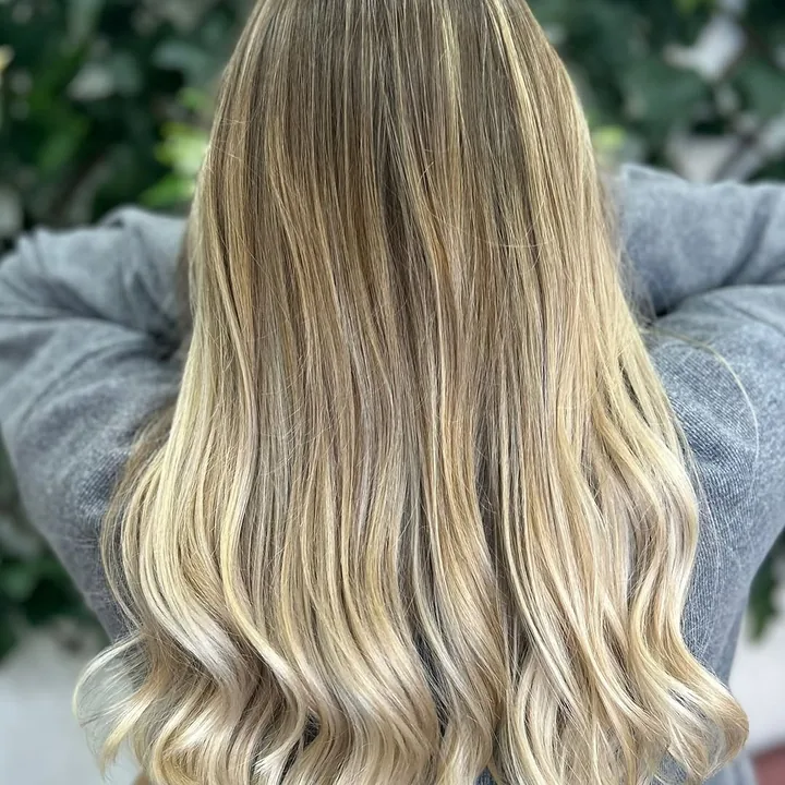 Melena larga con balayage rubio en ondas, de espaldas, ante la pared de hiedra del sal&oacute;n